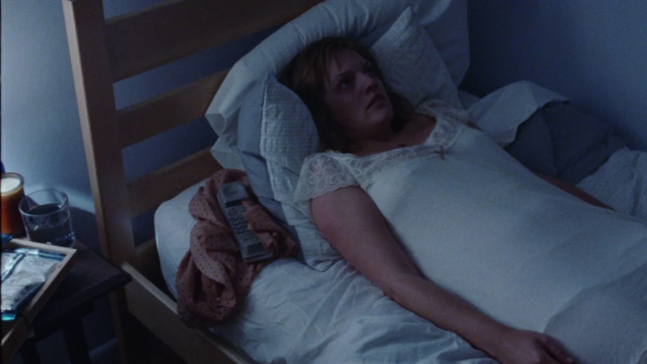 Queen of Earth (2015) movie still: medium — A person lies on a simple bed with a wooden headboard and white sheets. A small wooden table next to the…