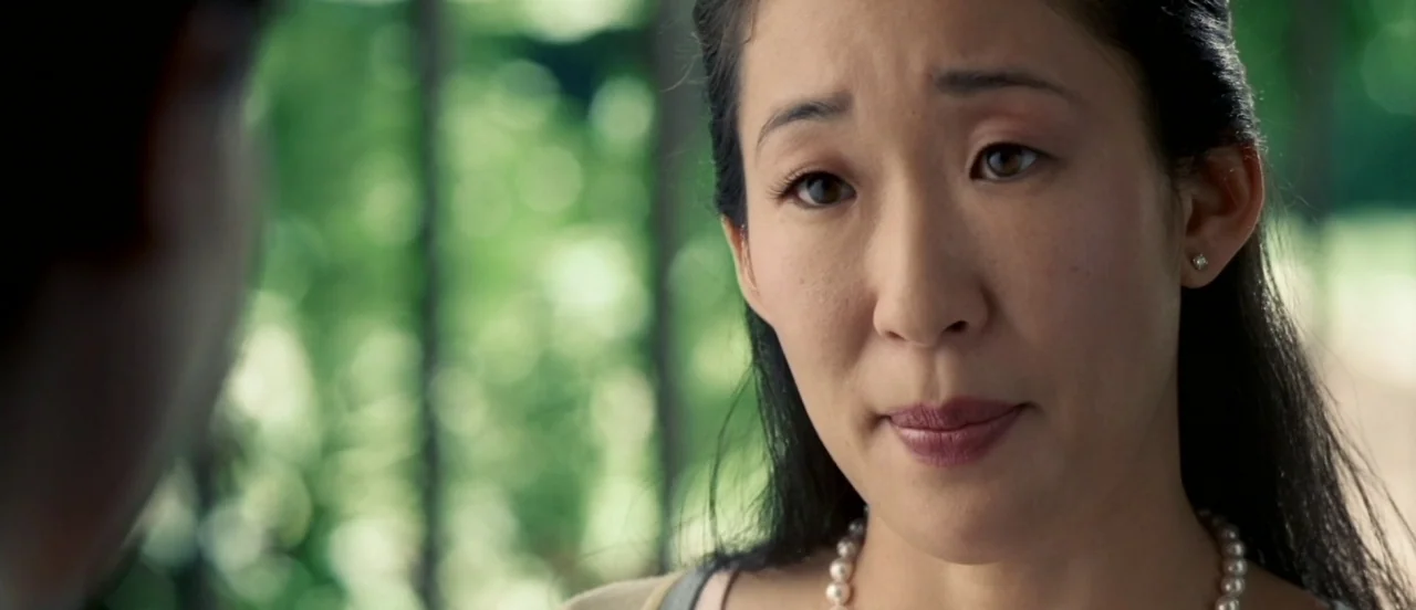 Hard Candy (2005) movie still: closeup — A woman stands in a lush green park with trees softly blurred in the background. She listens intently to a…
