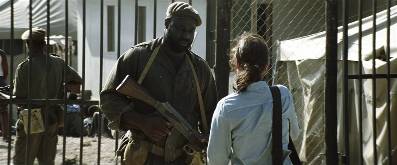 Blood Diamond (2006) movie still: medium — A military checkpoint features a tall metal fence with a gate. A soldier holds a rifle while interacting…
