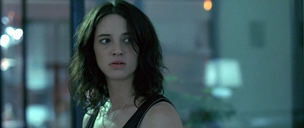 Boarding Gate (2007) movie still: closeup — A modern, dimly lit apartment interior with blurred lights in the background. A young woman with dark…