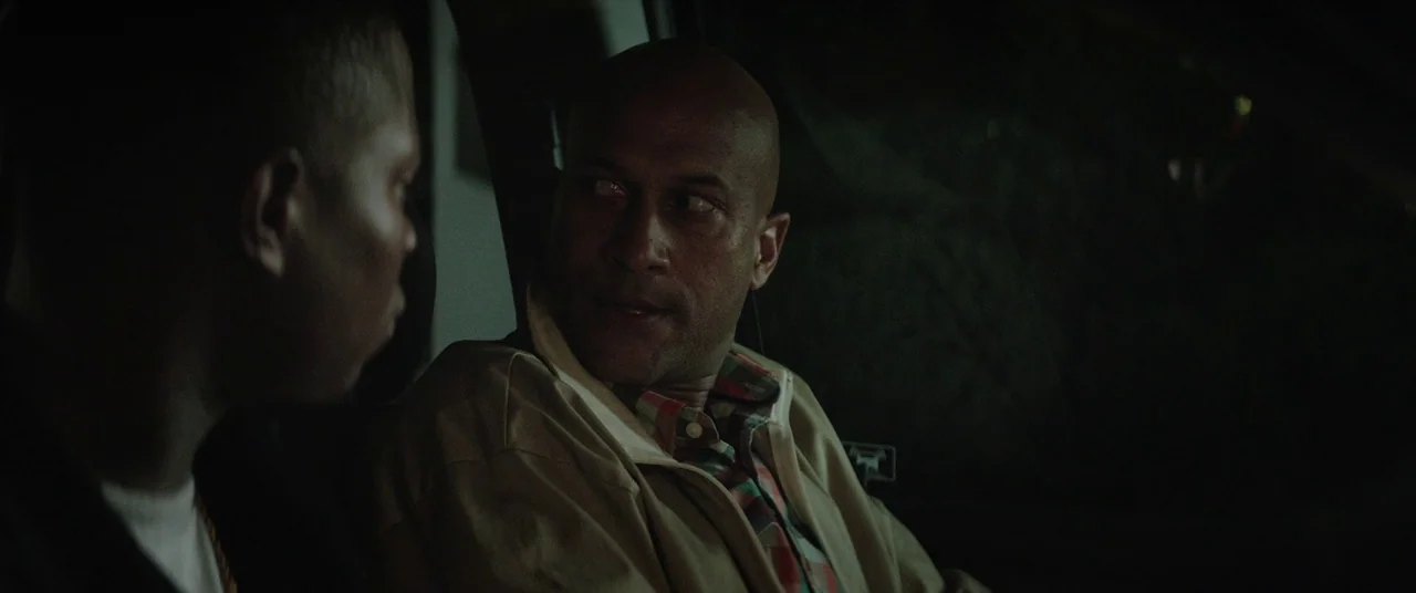 Keanu (2016) movie still: medium — The interior of a vehicle at night with two men in conversation. A bald man in a tan jacket faces another man…