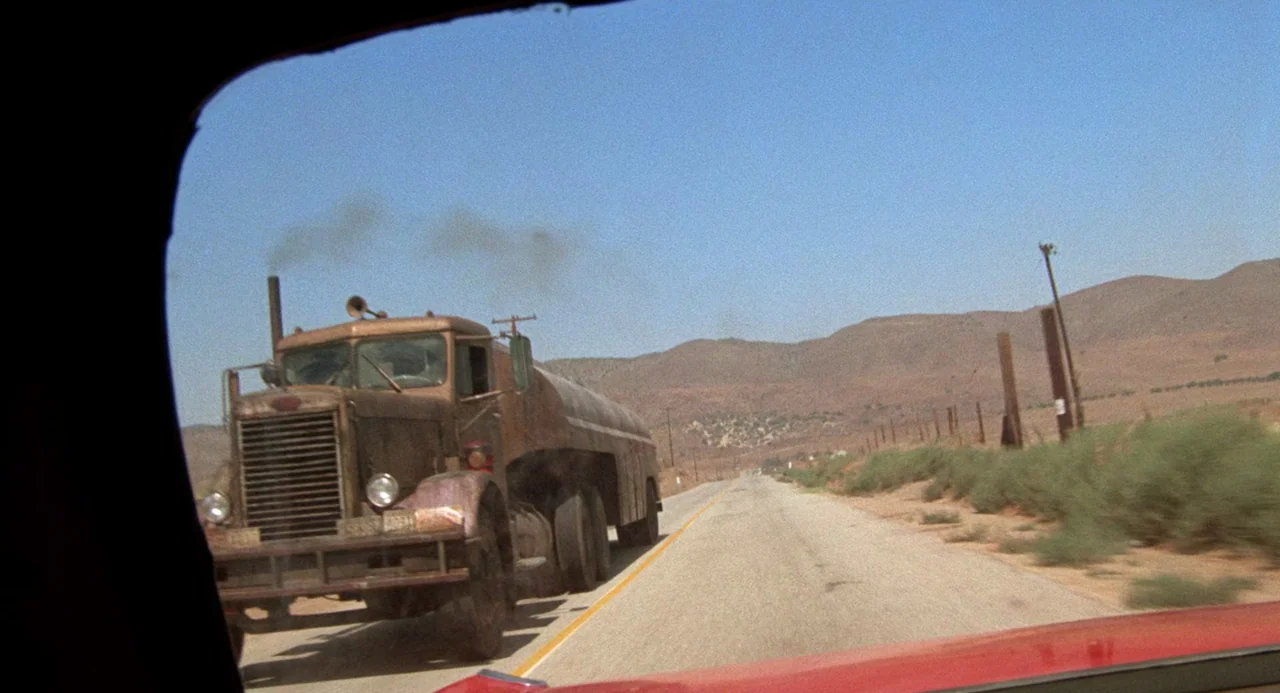 Duel (1971) movie still: wide — A rusted, dirty tanker truck occupies the side of a vast, arid highway. The scene is viewed from inside another…