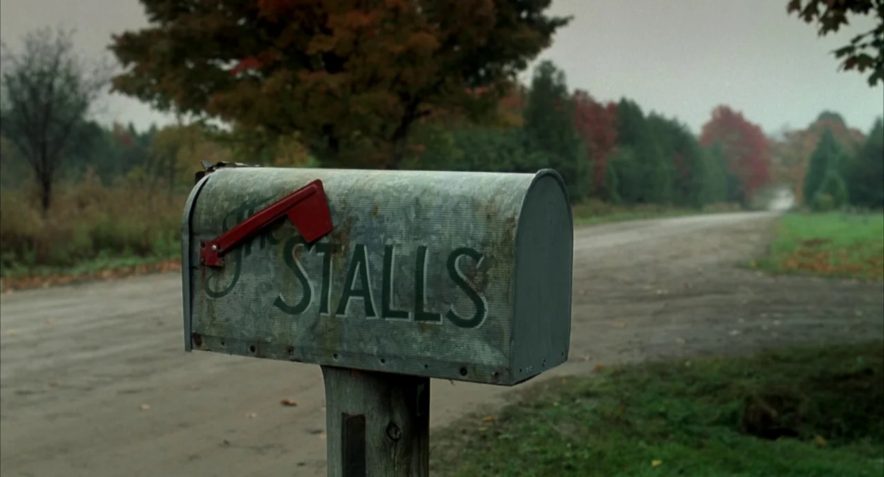 A History of Violence (2005) movie still: closeup — A metal mailbox with the name STALLS painted on it sits on a wooden post. A gravel road…