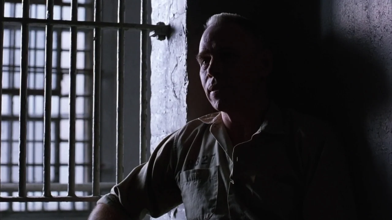 The Shawshank Redemption (1994) movie still: medium — A stone cell interior features thick vertical metal bars blocking a daylight window source. A…