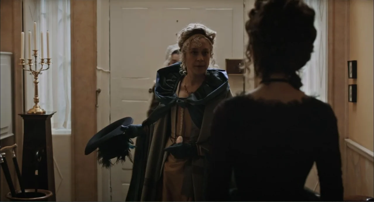 Love & Friendship (2016) movie still: medium — An interior residential foyer features light-colored walls, a closed door, and a candle holder. A…