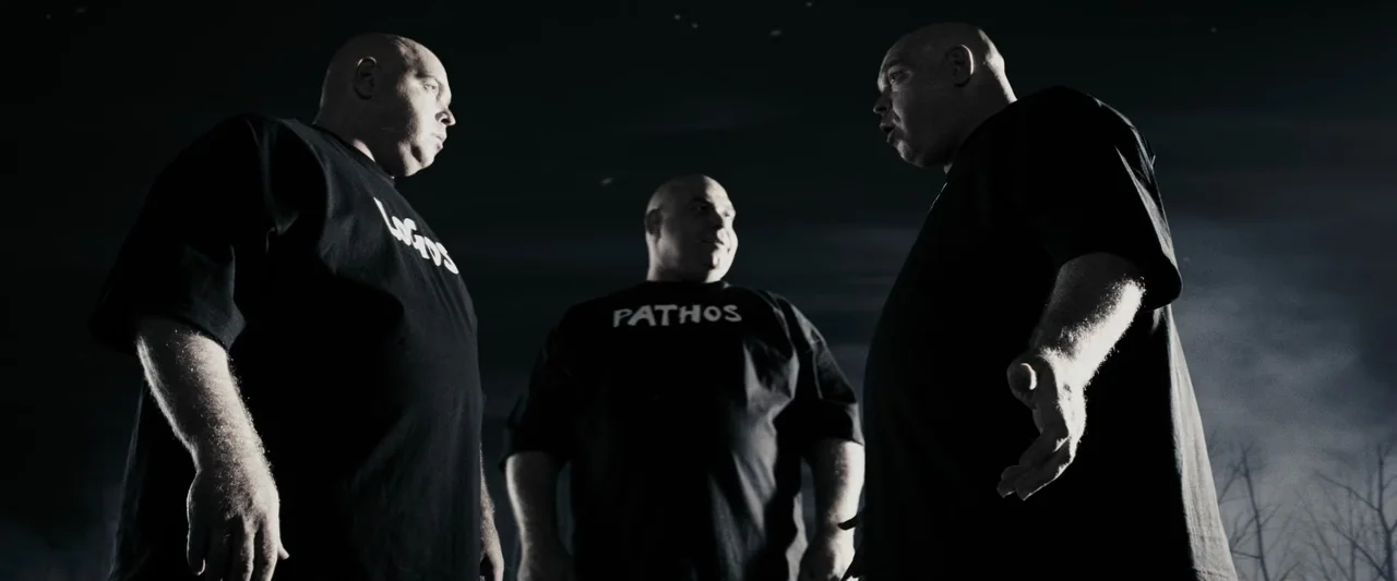 The Spirit (2008) movie still: medium — Three stout, bald men stand in a dark outdoor setting at night. They wear black t-shirts printed with Greek…