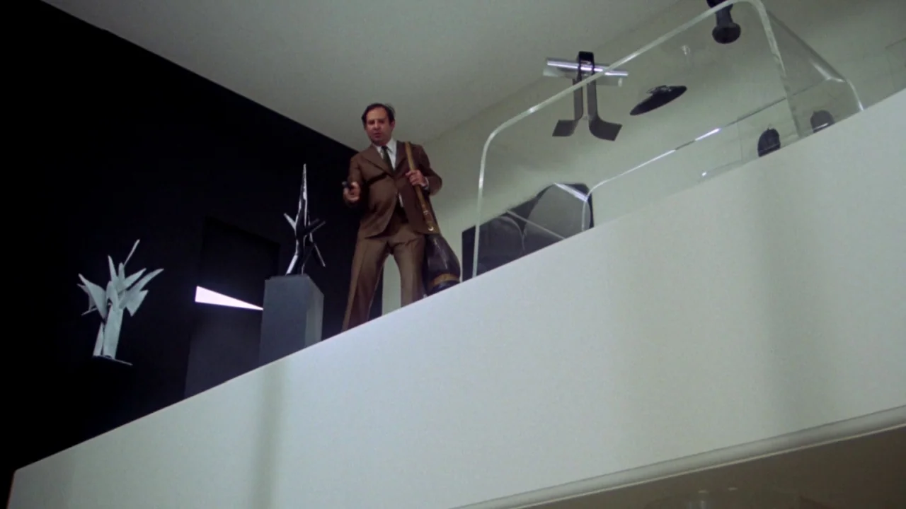 What’s Up, Doc? (1972) movie still: fullbody — A minimalist white mezzanine overlooks a floor with sharp black walls and abstract art. A man in a…