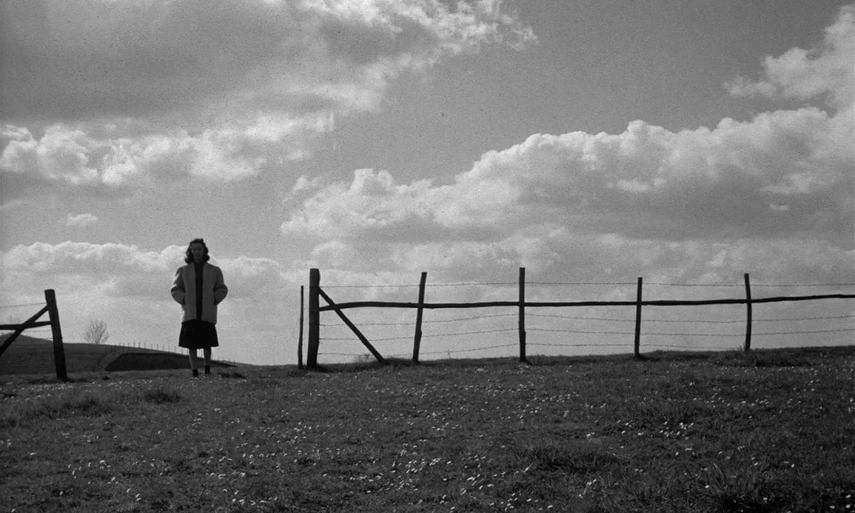 Léon Morin, Priest (1961) movie still: wide — A wide grassy hill under a large sky with patchy cumulus clouds. A woman stands stationary in the left…