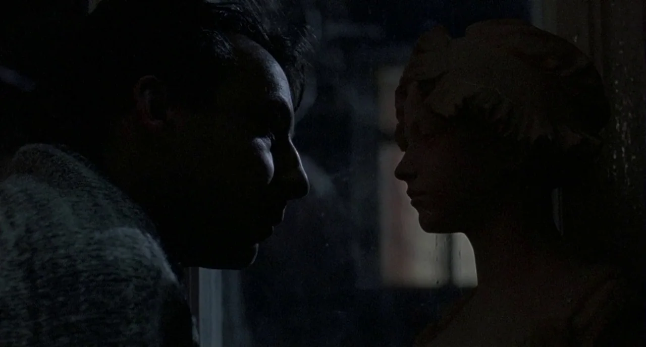 Three Colours: White (1994) movie still: medium — A dimly lit indoor space is occupied by a man and a stone bust. The man stands in close proximity…