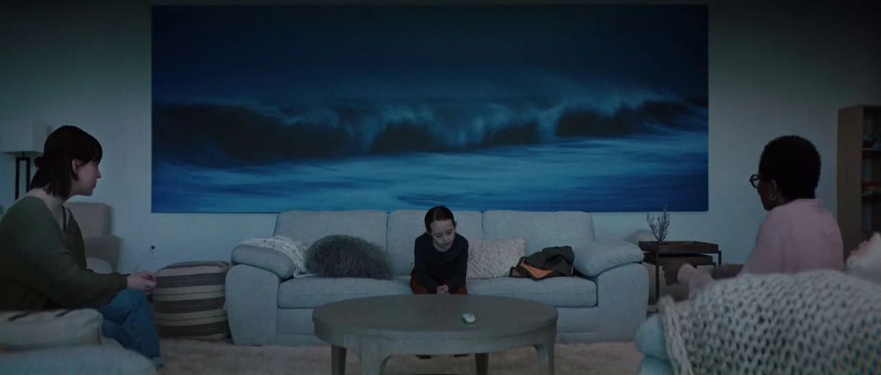 The Boogeyman (2023) movie still: wide — A living room features a large, dark ocean wave wall print behind a sofa. Three individuals sit separated…