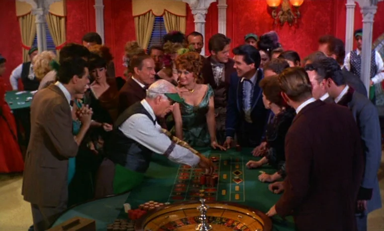 Frankie and Johnny (1966) movie still: medium — A crowded interior casino room features red damask walls and green roulette table felt. People in…