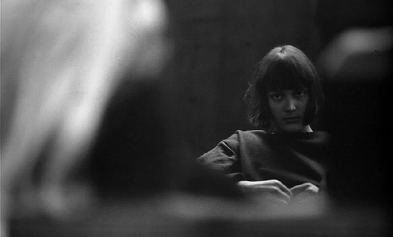 Stereo (1969) movie still: medium — A dimly lit room holds a person with dark hair looking into the distance. The subject sits in the background…