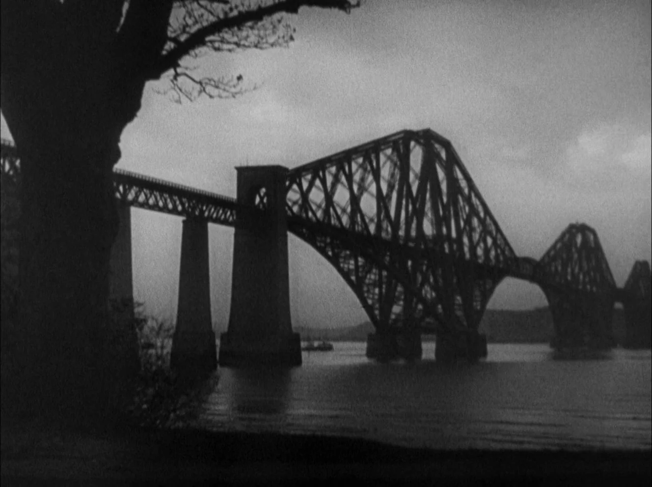 The 39 Steps (1935) movie still: establishing — The Forth Bridge spans a wide body of water under a flat overcast sky. A large tree silhouette…