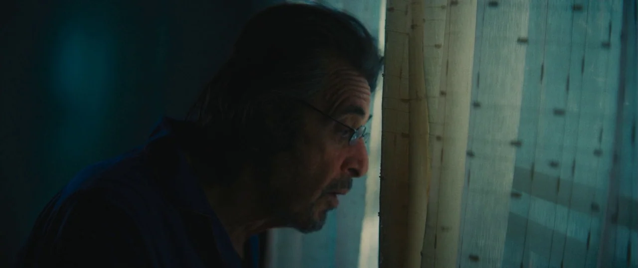 Manglehorn (2014) movie still: closeup — A dimly lit room features a sheer window curtain that catches soft exterior light. An elderly man presses…