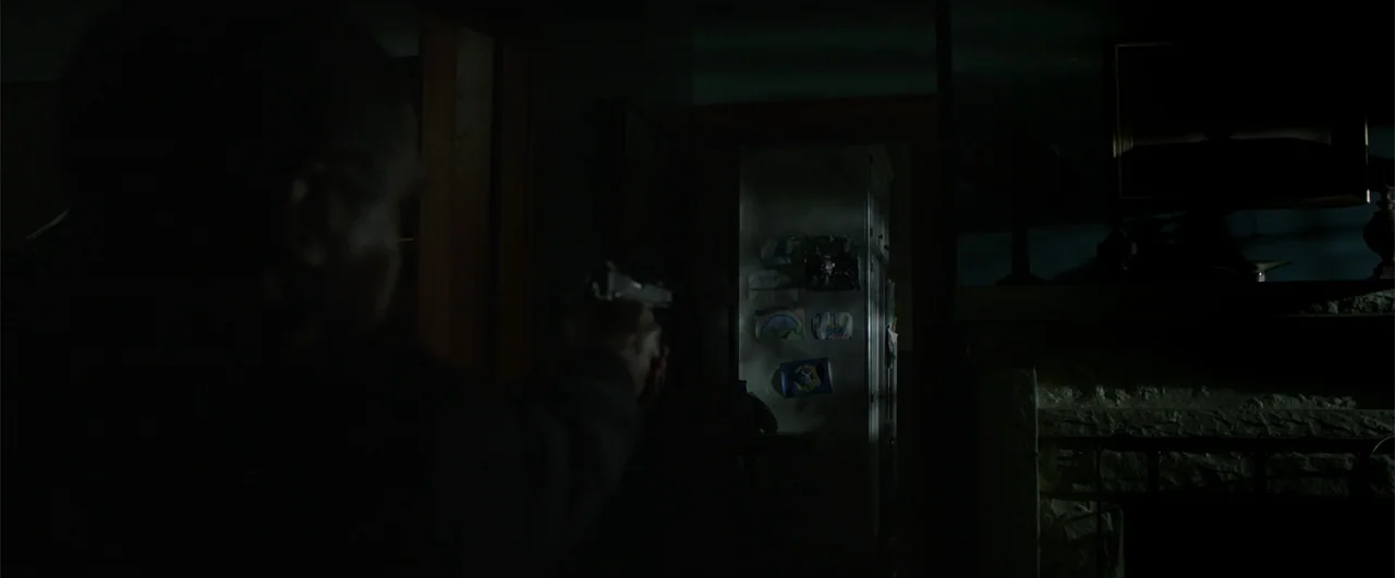 Lights Out (2016) movie still: medium — A dimly lit residential interior features a dark foreground with a illuminated doorway. An out of focus…