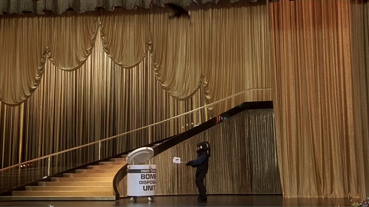 Naked Gun 33⅓: The Final Insult (1994) movie still: wide — A theatrical stage features sweeping gold fabric curtains draped behind a curved…