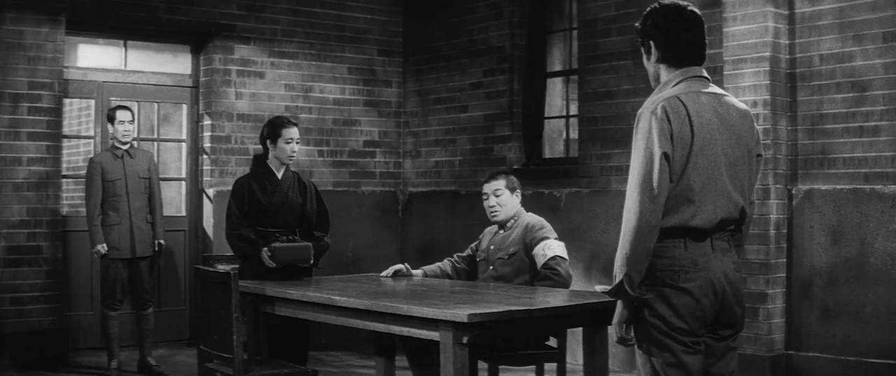 The Human Condition I: No Greater Love (1959) movie still: wide — A stark room features bare brick walls and a single wooden table. Four individuals…