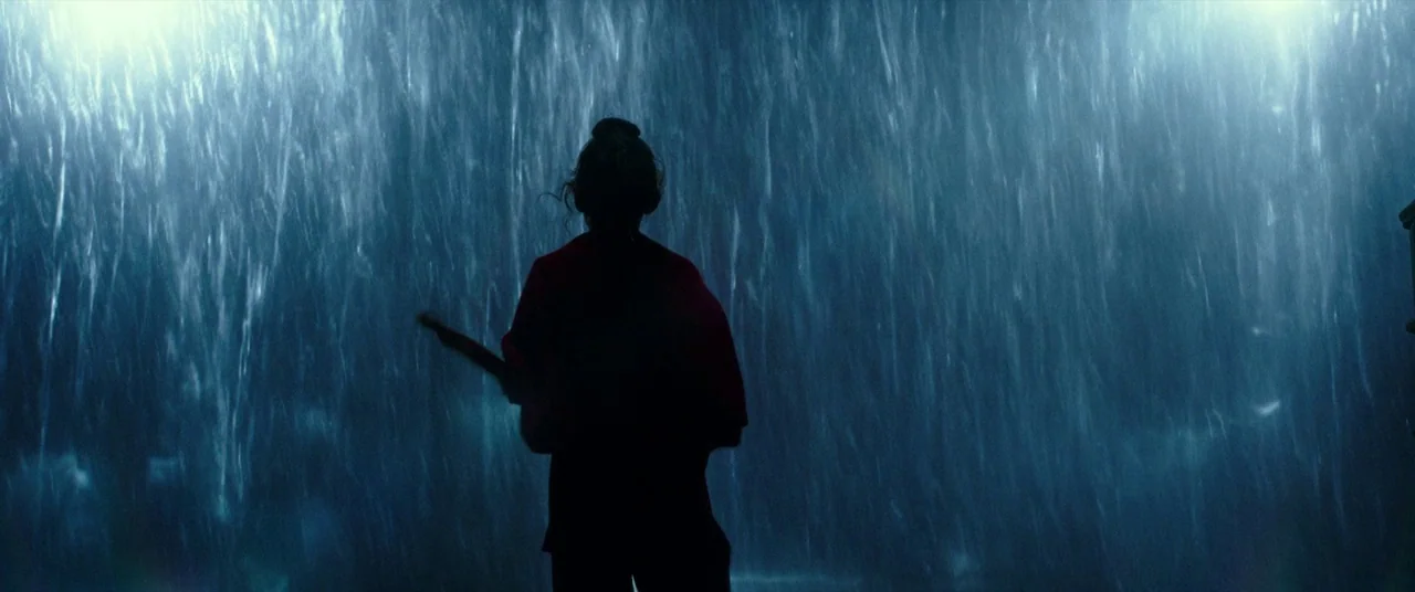 Godzilla Vs. Kong (2021) movie still: medium — A person stands in the center of a dark city street during a rainstorm. Rain streaks across the frame…
