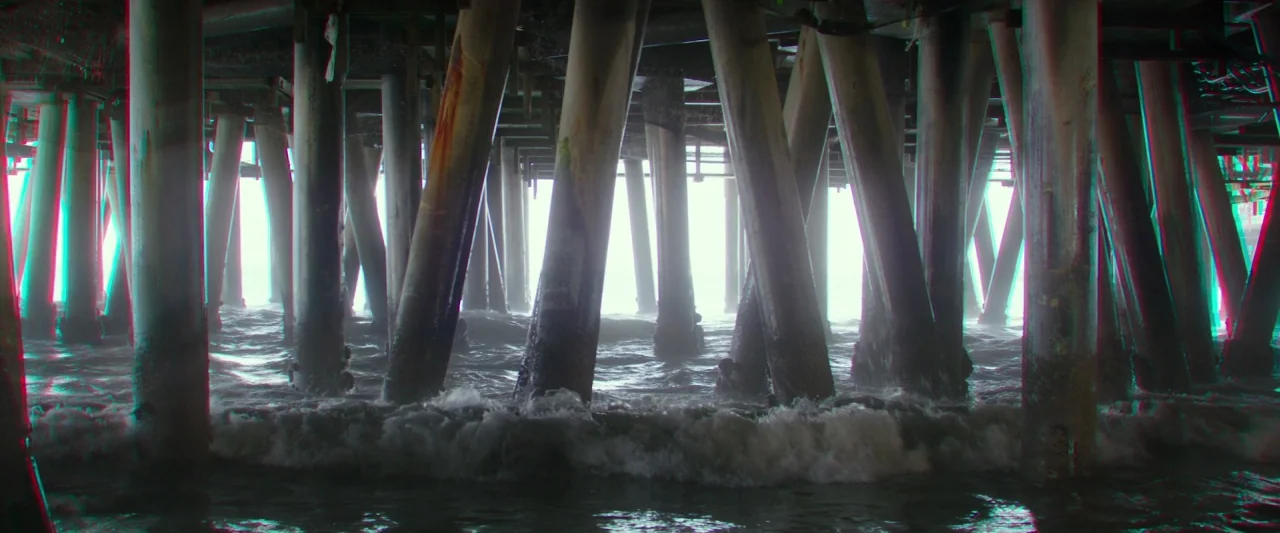 Hotel Artemis (2018) movie still: wide — Massive wooden support piles of a pier rise vertically from the choppy ocean water. Waves crash against the…