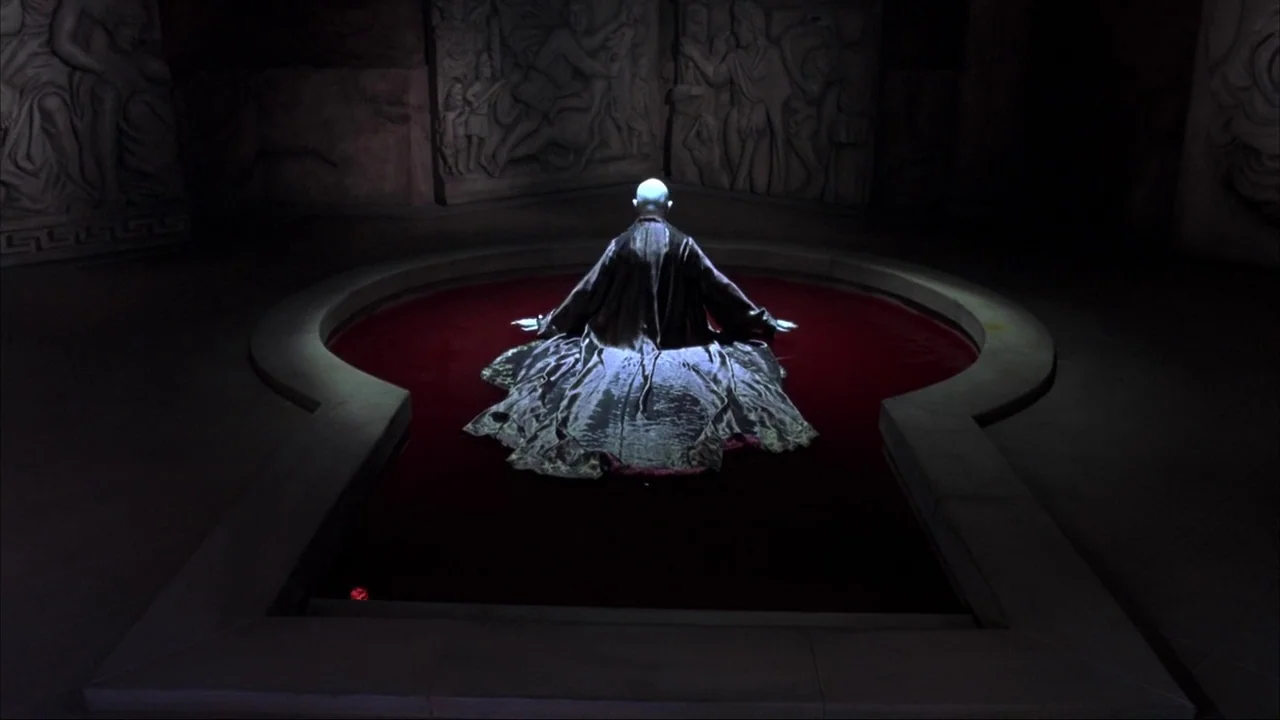Blade II (2002) movie still: wide — A dark subterranean chamber features stone walls with ancient relief carvings surrounding a central basin. A…