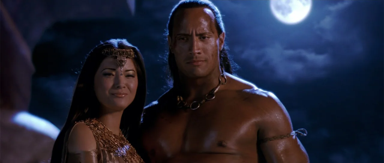 The Scorpion King (2002) movie still: medium — A dark outdoor environment is lit by a large full moon in the background. A muscular man and an…