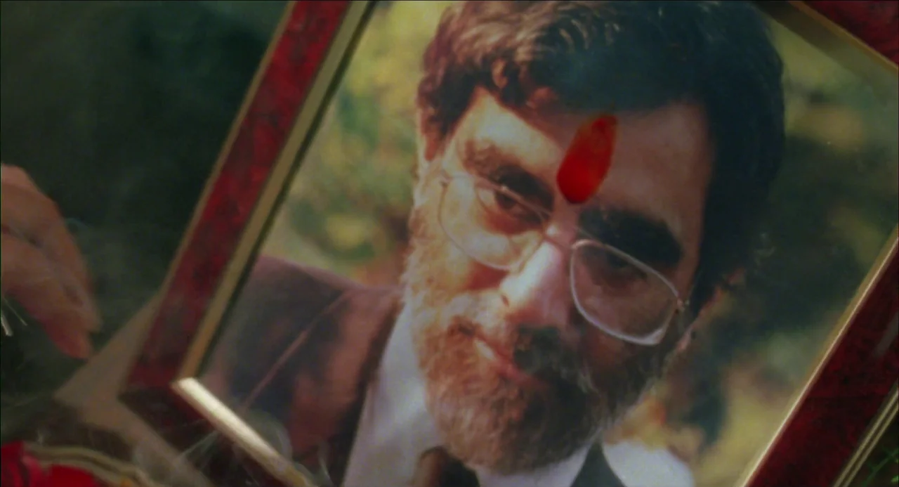 Monsoon Wedding (2001) movie still: closeup — A close-up shot of a framed photograph held in someone's hands. The photograph depicts a man with a…
