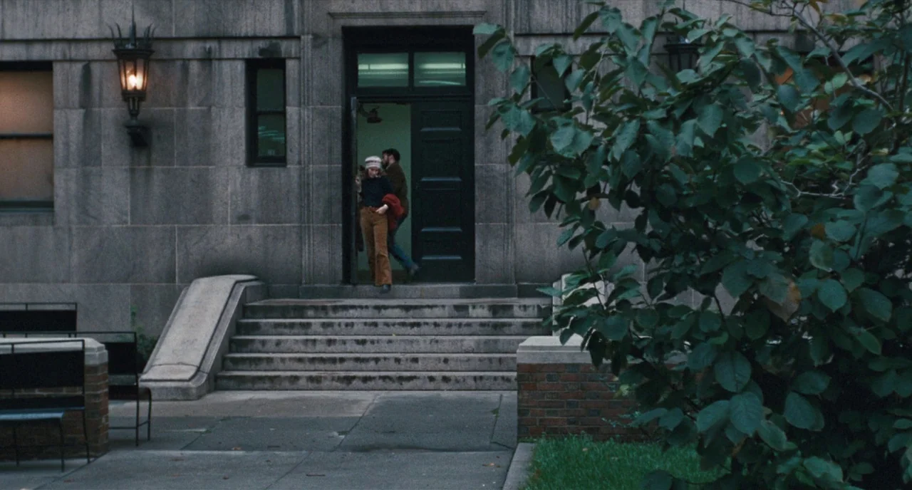 The Panic in Needle Park (1971) movie still: wide — A stone building with a dark door and ornate lamp sits above concrete stairs. Two people walk…