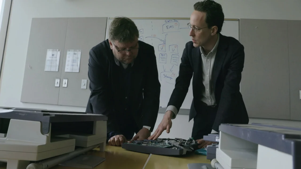 Kill Chain: The Cyber War on America's Elections (2020) movie still: medium — A bright office features a whiteboard with diagrams and two printers…