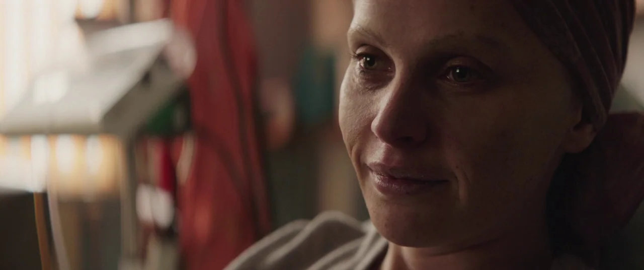 A Monster Calls (2016) movie still: closeup — A hospital room with a medical device visible in the blurred background. A woman in a head covering…