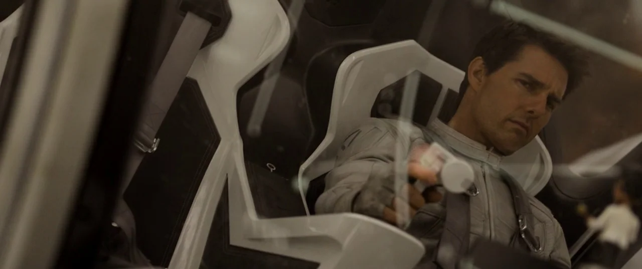 Oblivion (2013) movie still: medium — A high-tech pilot seat with glossy white plastic framing and black textured padding. The man operates a small…