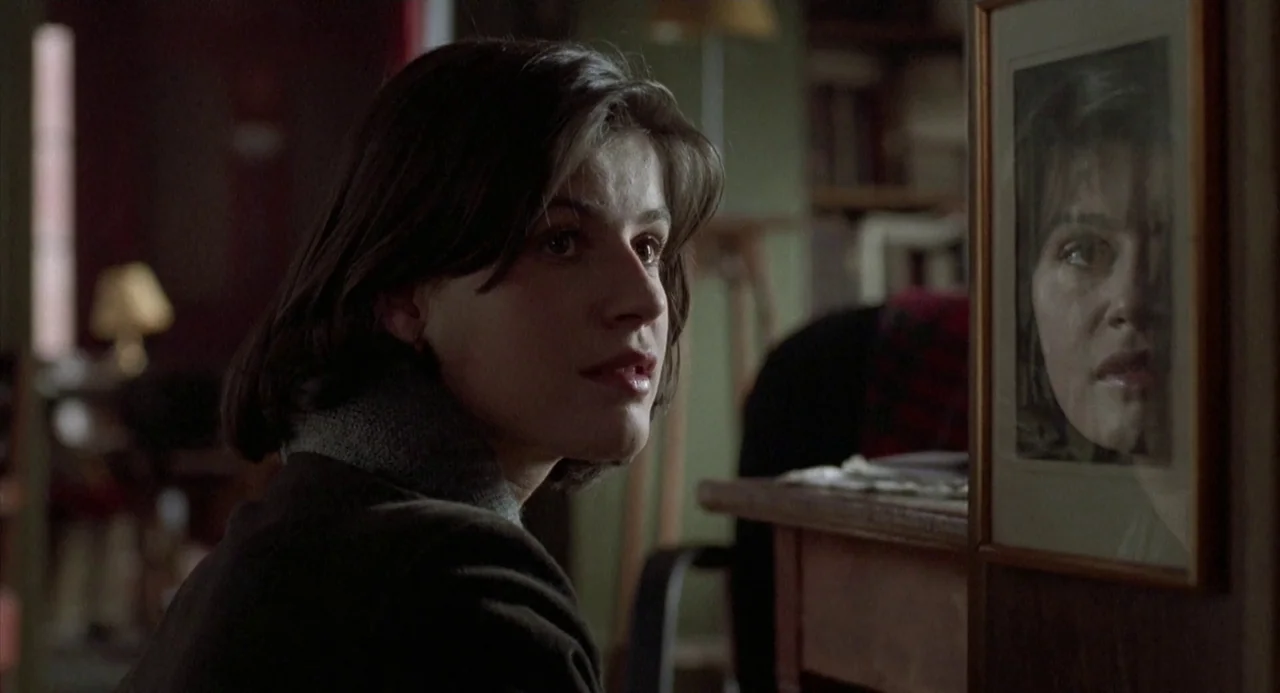 Three Colours: Red (1994) movie still: medium — A dimly lit room with muted green walls and a wooden writing desk. A young woman turns her head to…