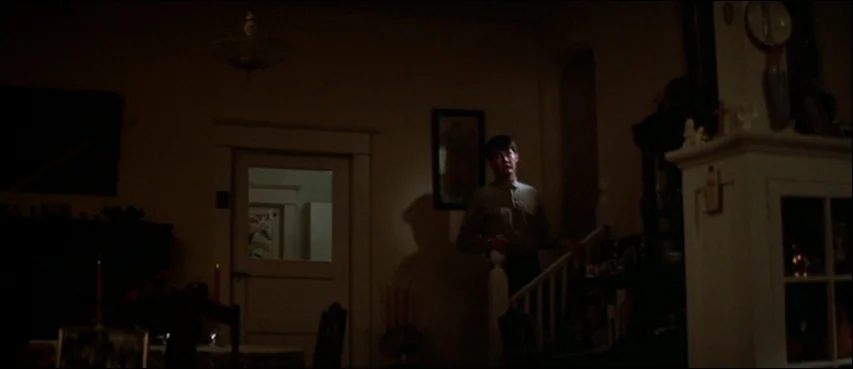 Blue Velvet (1986) movie still: medium — A dimly lit domestic interior features a staircase and wooden accents. A young man stands on the stairs…