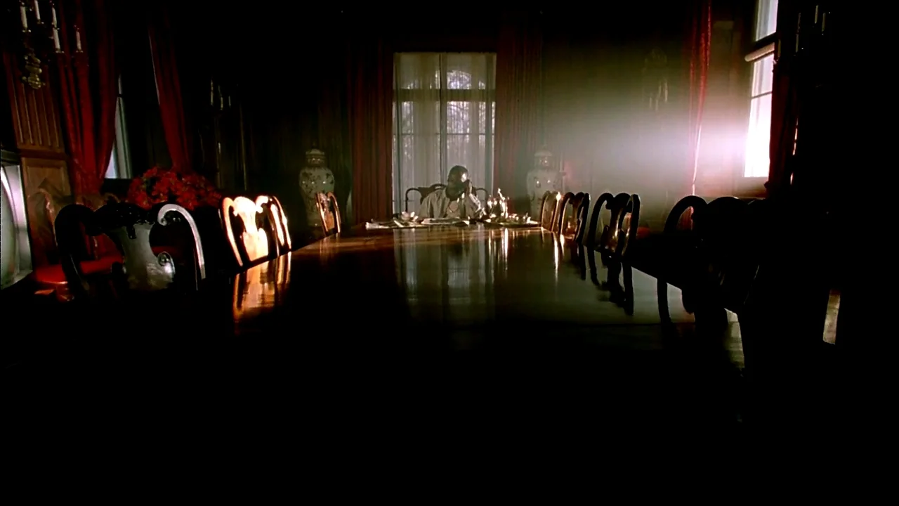 Belly (1998) movie still: wide — A dark, wood-paneled room features a massive dining table and deep red curtains. A solitary man sits at the far end…