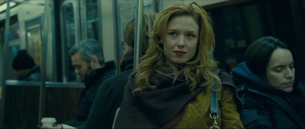 Shame (2011) movie still: medium — A dimly lit passenger train car features rows of seating and chrome support poles. A woman with blonde hair sits…