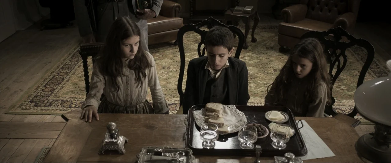 Fatima (2020) movie still: medium — A dark wood-paneled room features a vintage rug and formal chairs around a table. Three children sit quietly at…
