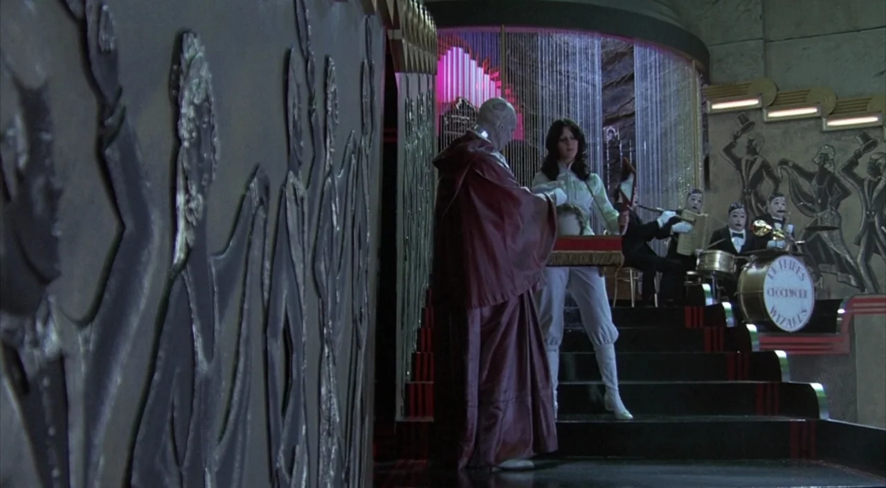 Dr. Phibes Rises Again (1972) movie still: wide — A stylized nightclub interior features walls adorned with brass relief sculptures of dancing…