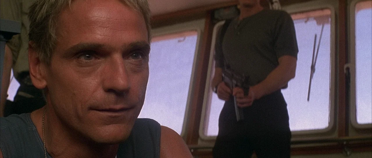 Die Hard with a Vengeance (1995) movie still: medium — A cramped ship bridge interior with large windows looking out to a bright sky. A man in the…