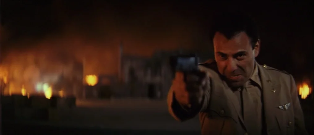 Catch 22 (1970) movie still: medium — A dark military base exterior is illuminated by large flickering fires in the distance. A man in a tan uniform…
