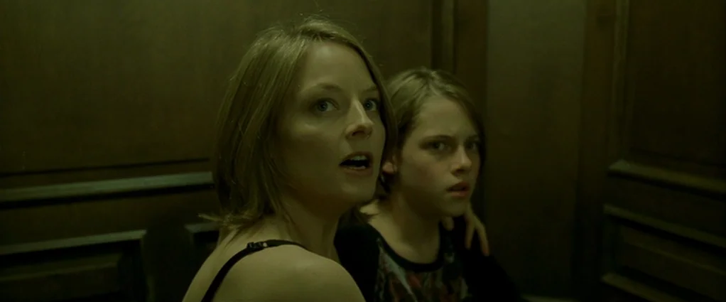 Panic Room (2002) movie still: medium — The interior walls of a dim wooden elevator paneling surround the two subjects. An adult woman and a young…