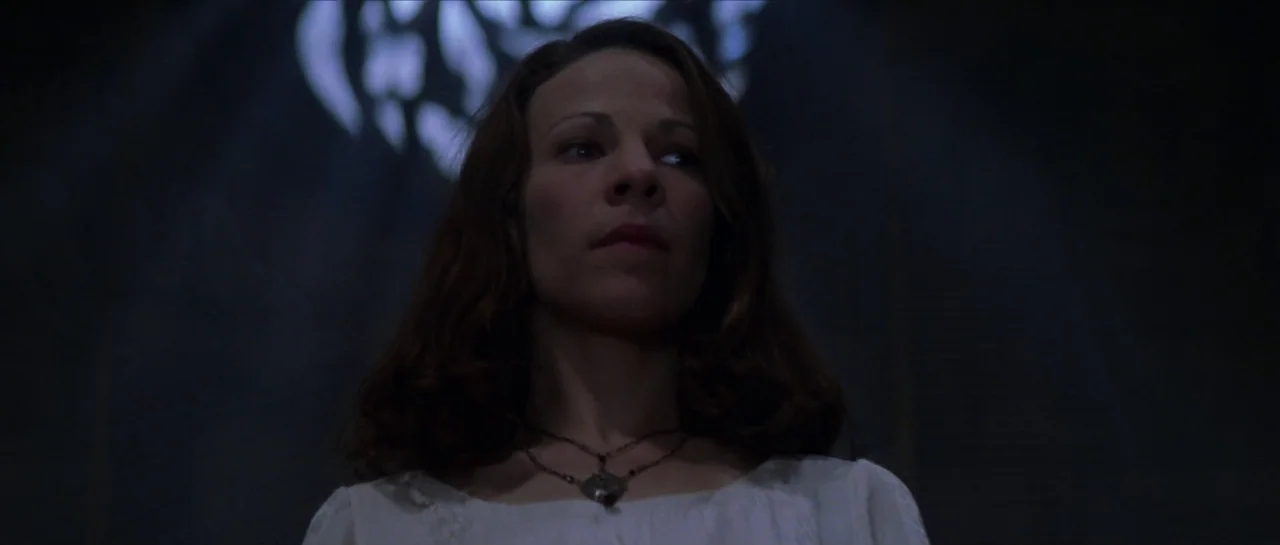 The Haunting (1999) movie still: closeup — A woman stands in a dimly lit, dark space with a diffuse overhead light source. She is positioned in…
