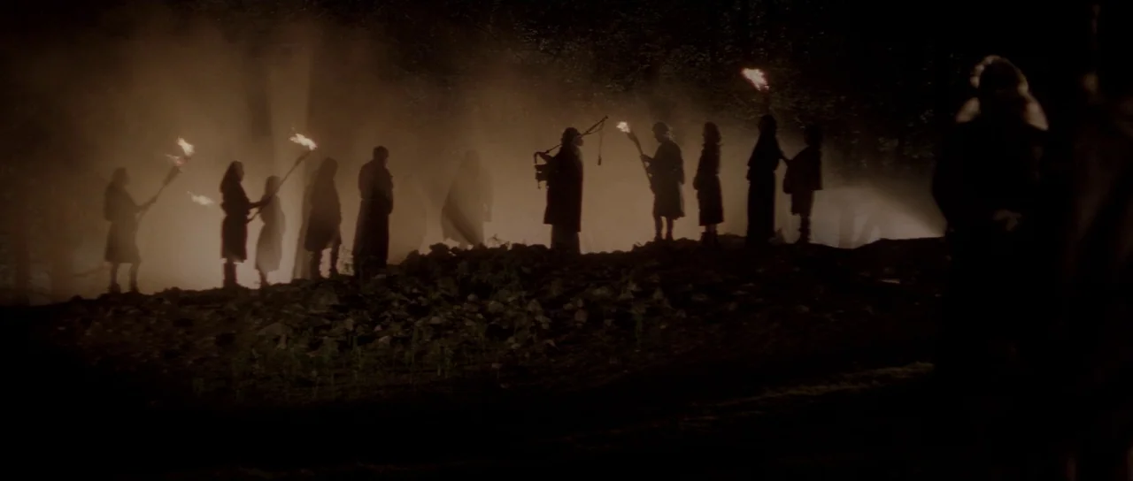 Braveheart (1995) movie still: wide — A group of cloaked figures stands along a ridge in a fog-covered wooded area. The people hold lit torches that…