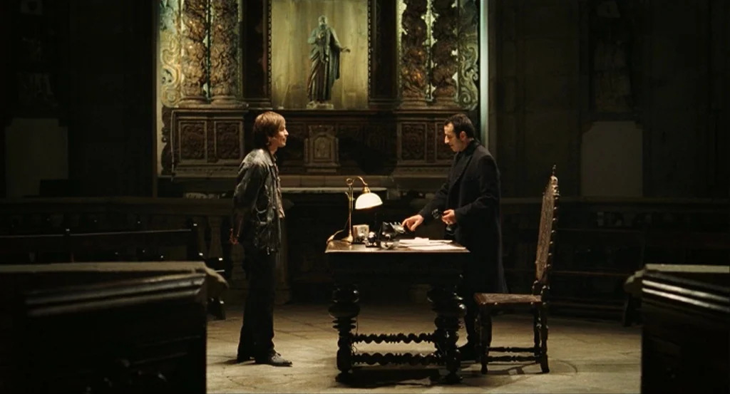 This Night (2008) movie still: wide — A stone interior with wooden pews and a centrally placed carved wooden desk. Two men converse while one…