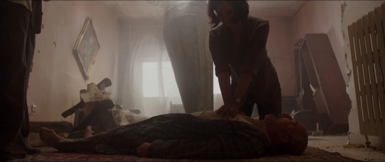Under The Shadow (2016) movie still: medium — A dusty, damaged interior with peeling paint and a large metal object near the window. A woman kneels…