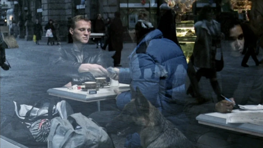 71 Fragments of a Chronology of Chance (1994) movie still: medium — An outdoor city sidewalk is reflected over a cafe table where two people sit. A…