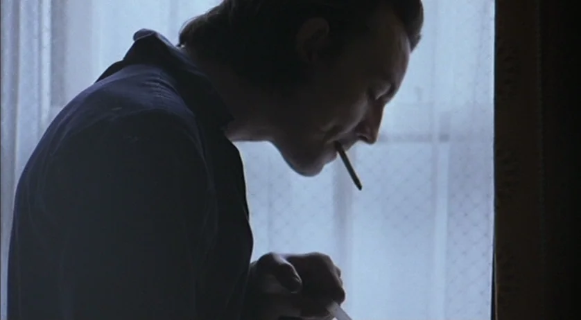 Ratcatcher (1999) movie still: medium — A dark-toned interior space features a person silhouetted against a sheer white curtain. A young man with a…