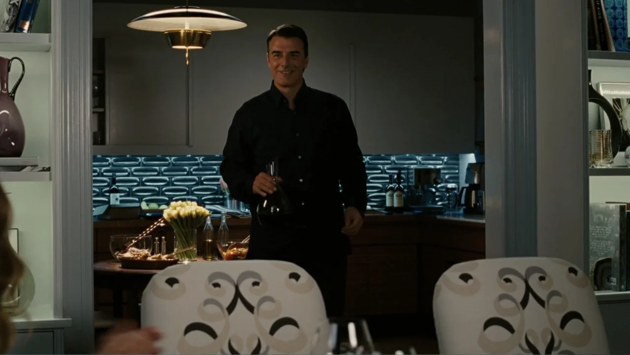 Sex and the City 2 (2010) movie still: medium — A modern home interior with a dark kitchen visible through a wide doorway. A man stands in the…