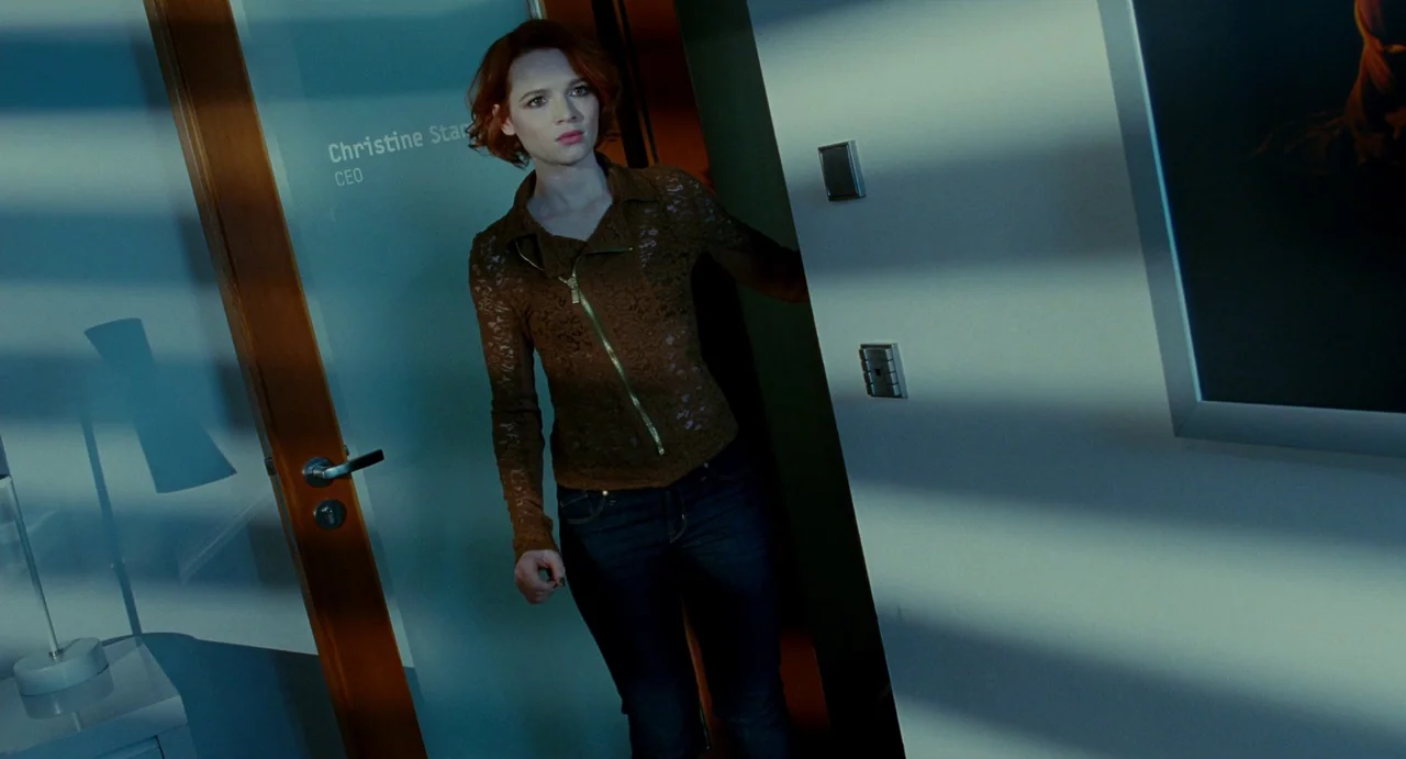 Passion (2012) movie still: medium — A modern professional workplace featuring frosted glass doors with printed name signage. A woman with short red…