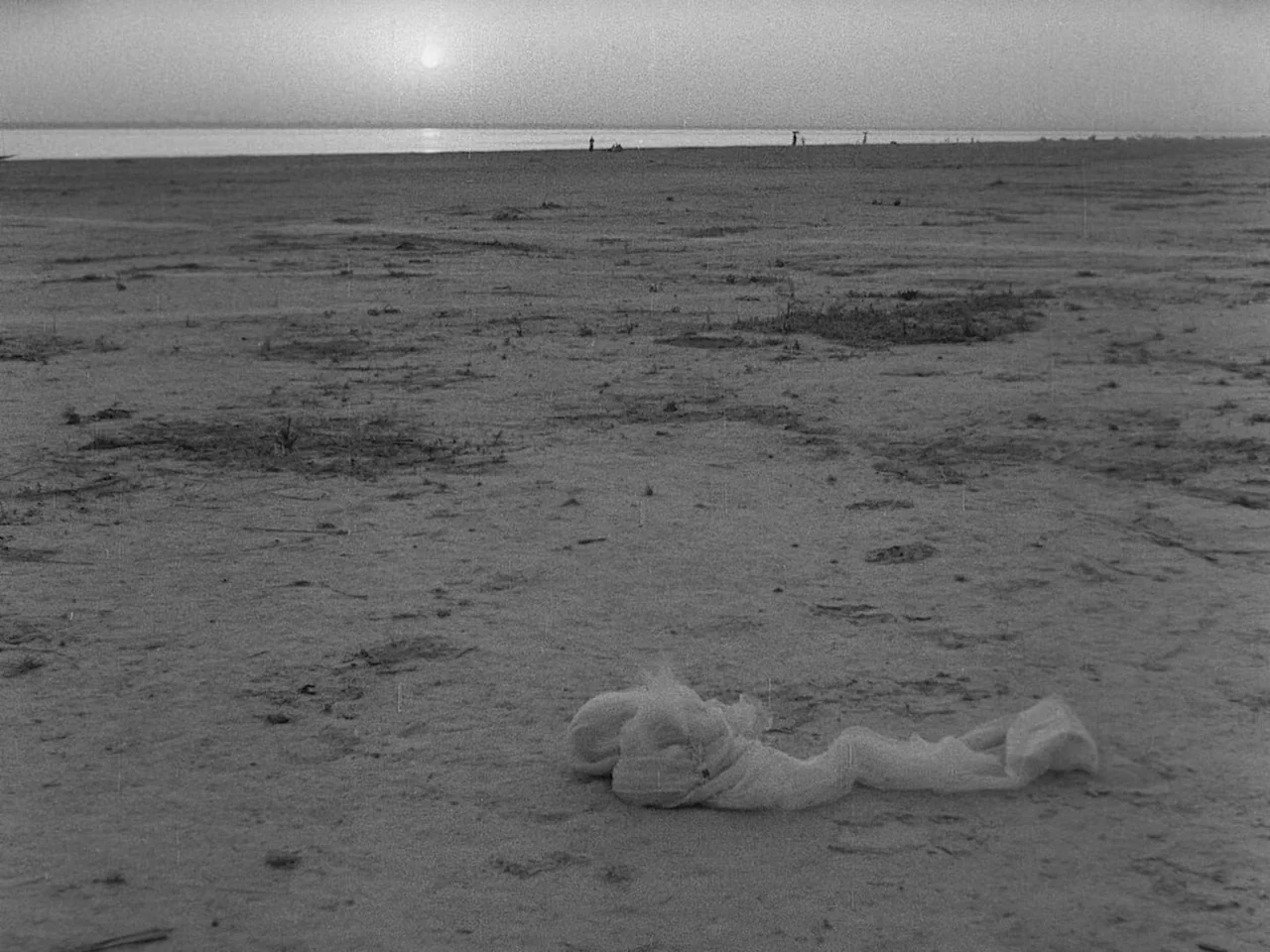 The Music Room (1958) movie still: establishing — A vast, barren sandy beach extends toward a distant horizon under a setting sun. A single white…