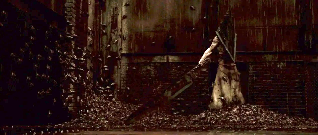 Silent Hill movie still: wide — A dark brick alleyway is cluttered with heaps of dark debris and swarming insects. A tall figure wearing a pyramid…