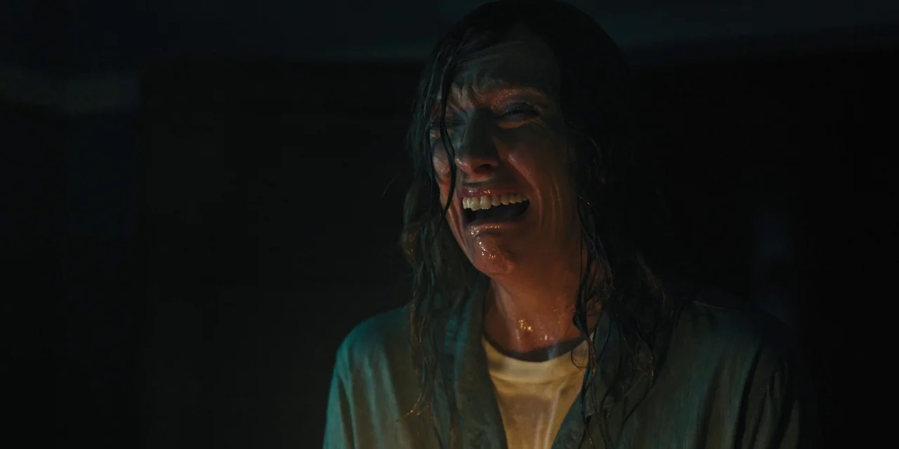 Hereditary (2018) movie still: closeup — A dark indoor setting provides a void-like backdrop for the subject. A woman in a shirt reacts with a cry.